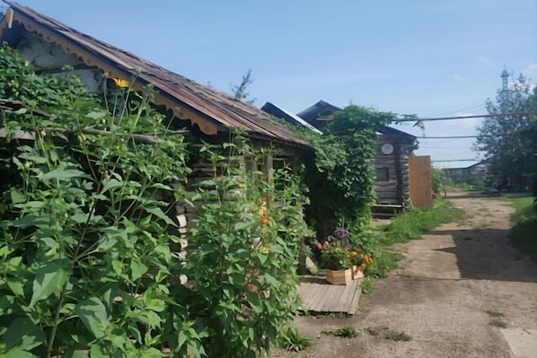 A rustic wooden house with a dirt path leading to it, surrounded by greenery. - Maluxia (Ergun)
