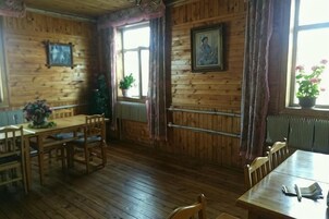 Un interior de madera con dos mesas de comedor, sillas, un árbol de Navidad y una ventana con cortinas.