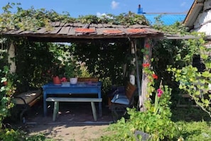 A rustic outdoor seating area with a table and benches, surrounded by greenery and a wooden structure. - Maluxia (Ergun)