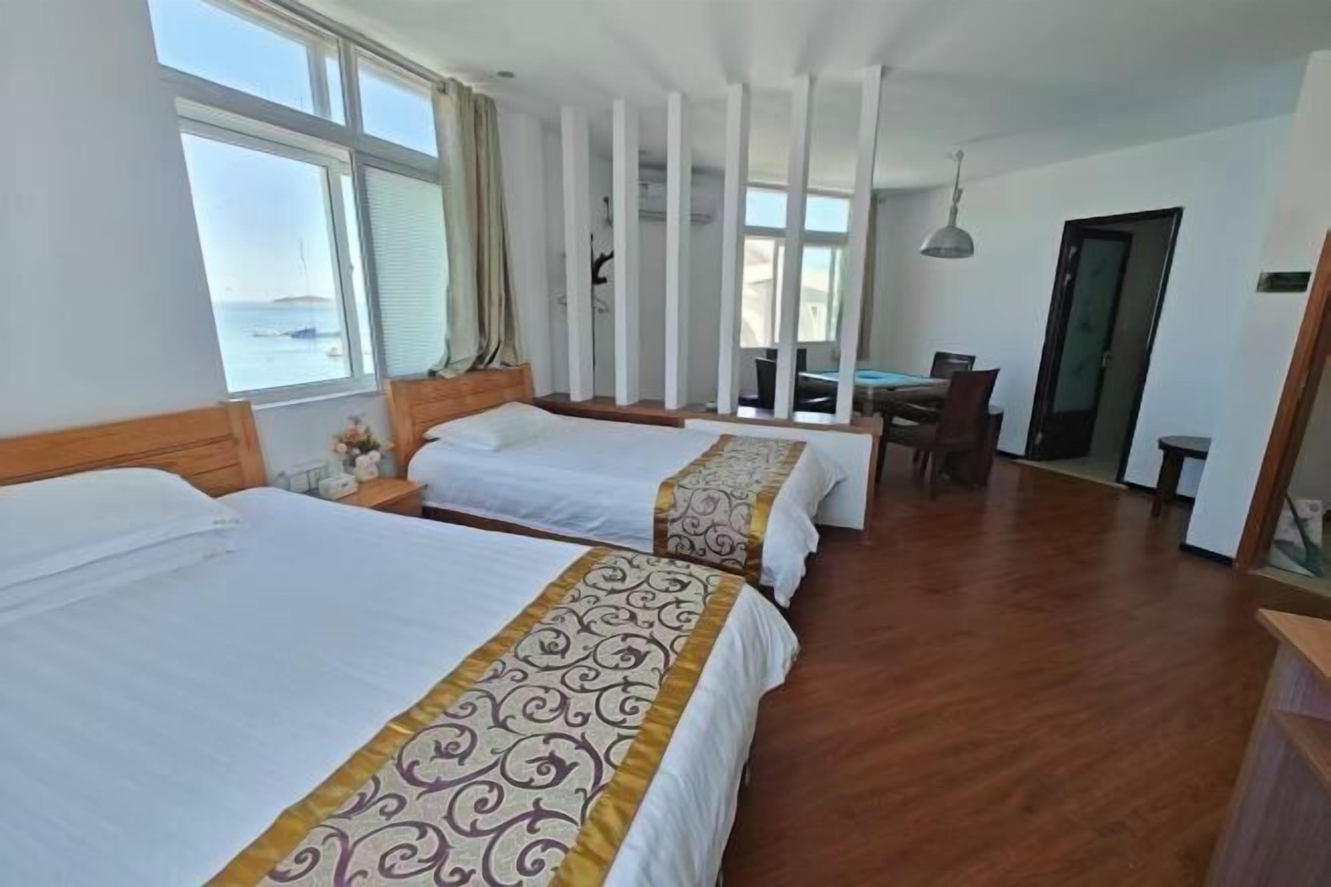 A hotel room with two beds, a dining table, and a view of the sea.