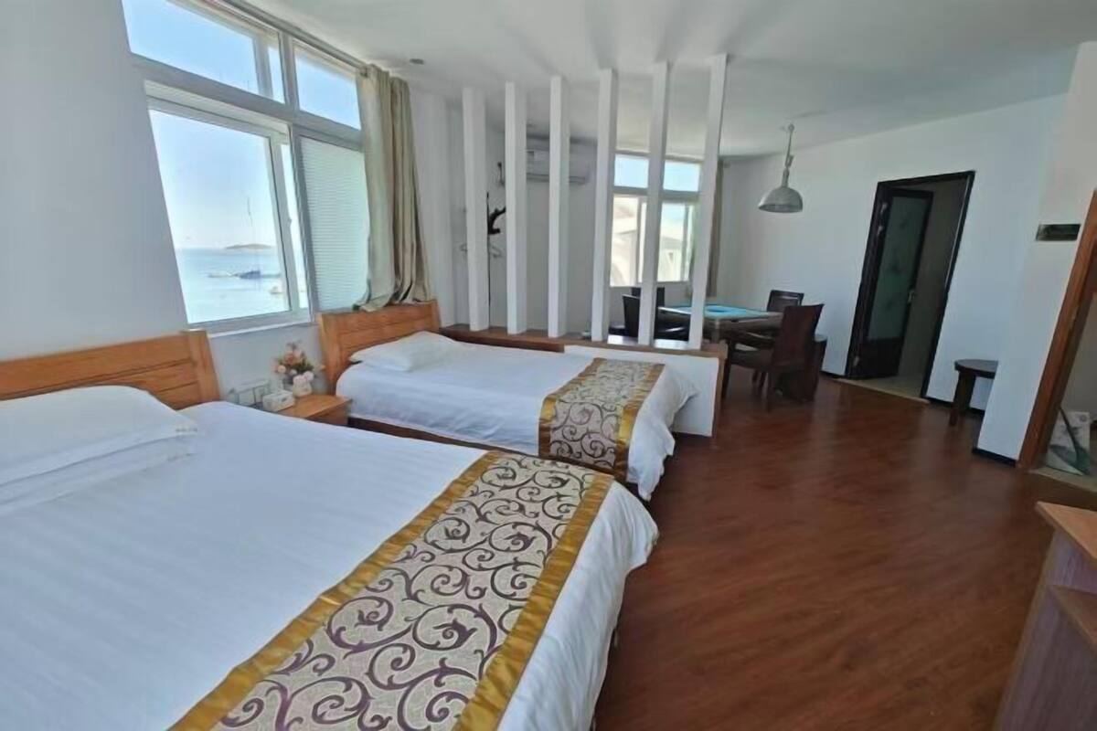 Een hotelkamer met twee bedden, een eettafel en uitzicht op zee.