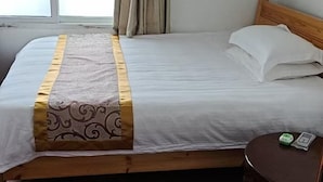 Een hotelkamer met een bed, een rond houten nachtkastje en een raam met gordijnen.