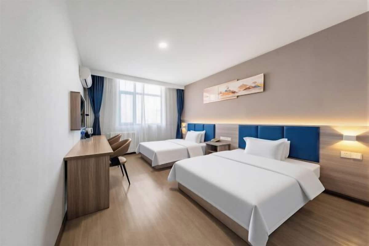 Une chambre d’hôtel avec deux lits, un bureau, une chaise, une fenêtre avec des rideaux et une œuvre d’art accrochée au mur.