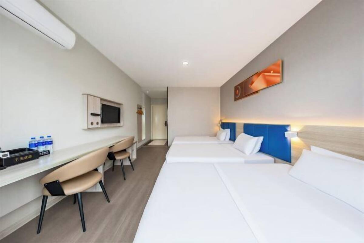 Une chambre d’hôtel avec deux lits, un bureau avec des chaises, une télévision et une œuvre d’art accrochée au mur.