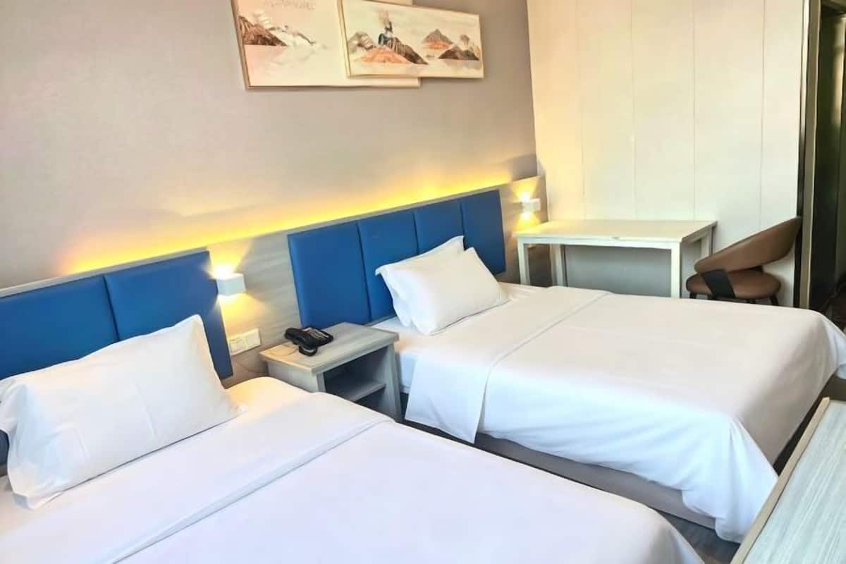 Une chambre d’hôtel avec deux lits, un bureau, une chaise et des œuvres d’art accrochées au mur.