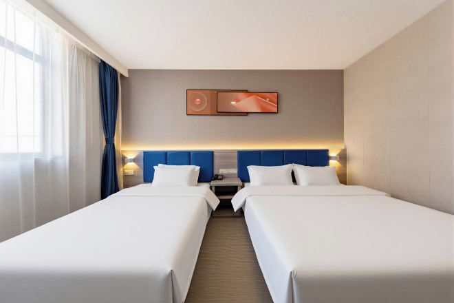 A hotel room with two beds, a headboard, a nightstand, and a wall-mounted TV.