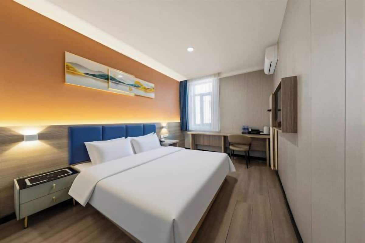 Une chambre d’hôtel avec un lit, une table de chevet, un bureau, une chaise et un tableau au mur.
