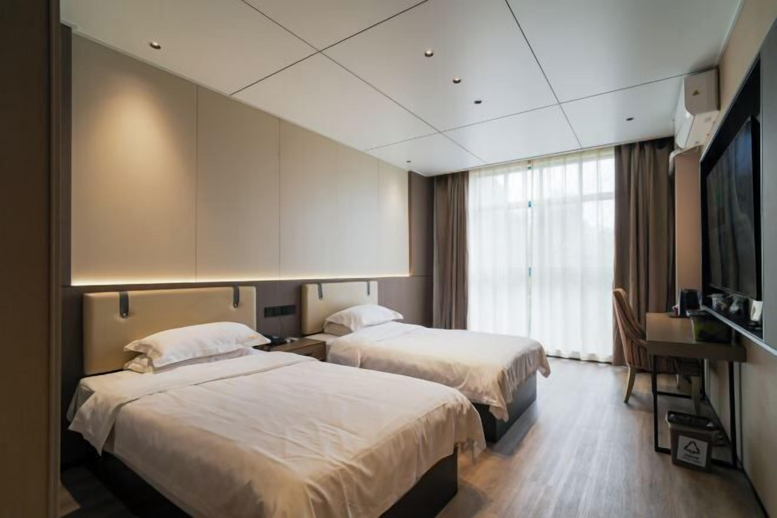 Een hotelkamer met twee bedden, een bureau, een stoel en een groot raam met gordijnen.