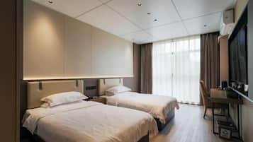 Een hotelkamer met twee bedden, een bureau, een stoel en een groot raam met gordijnen.