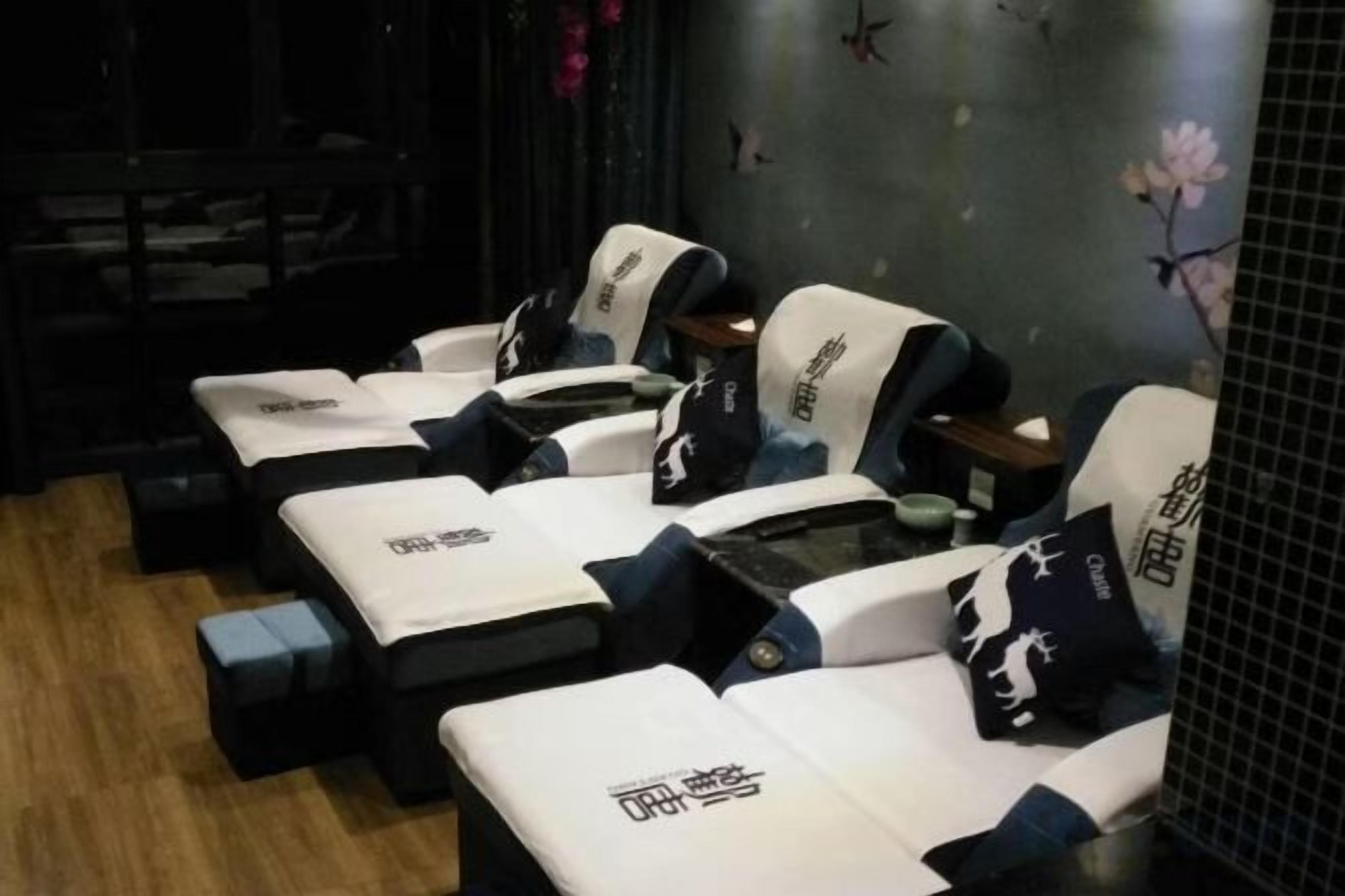 Une rangée de fauteuils de massage avec coussins, disposés dans une pièce dont le sol est sombre et un des murs est décoré de motifs floraux.