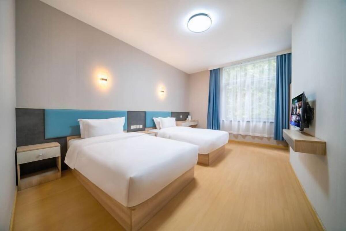 A hotel room with two beds, a TV, a desk, and a window with curtains.