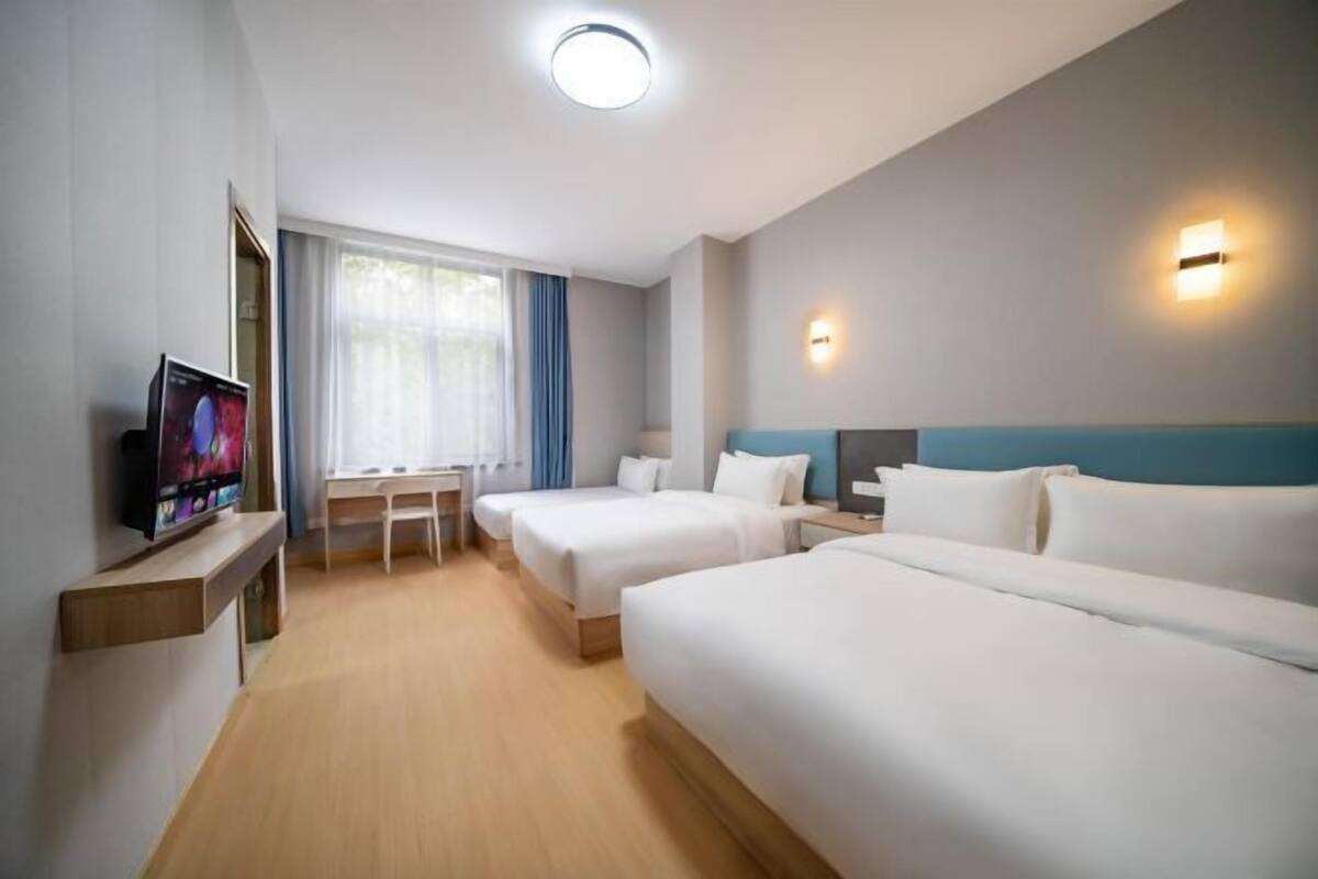 A hotel room with two beds, a desk, a TV, and a window with curtains.