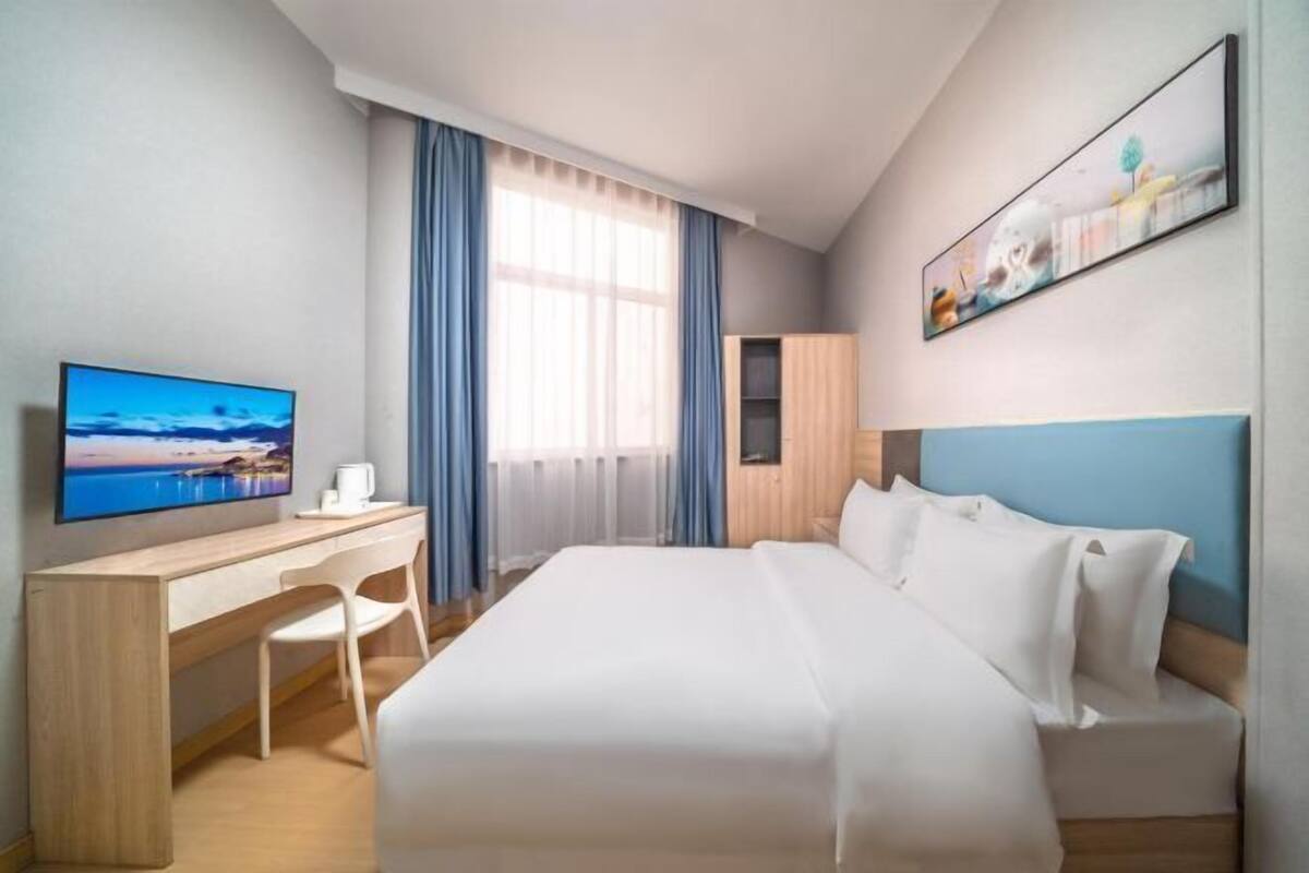 A hotel room with a bed, a desk, a chair, a television, and a window with curtains.
