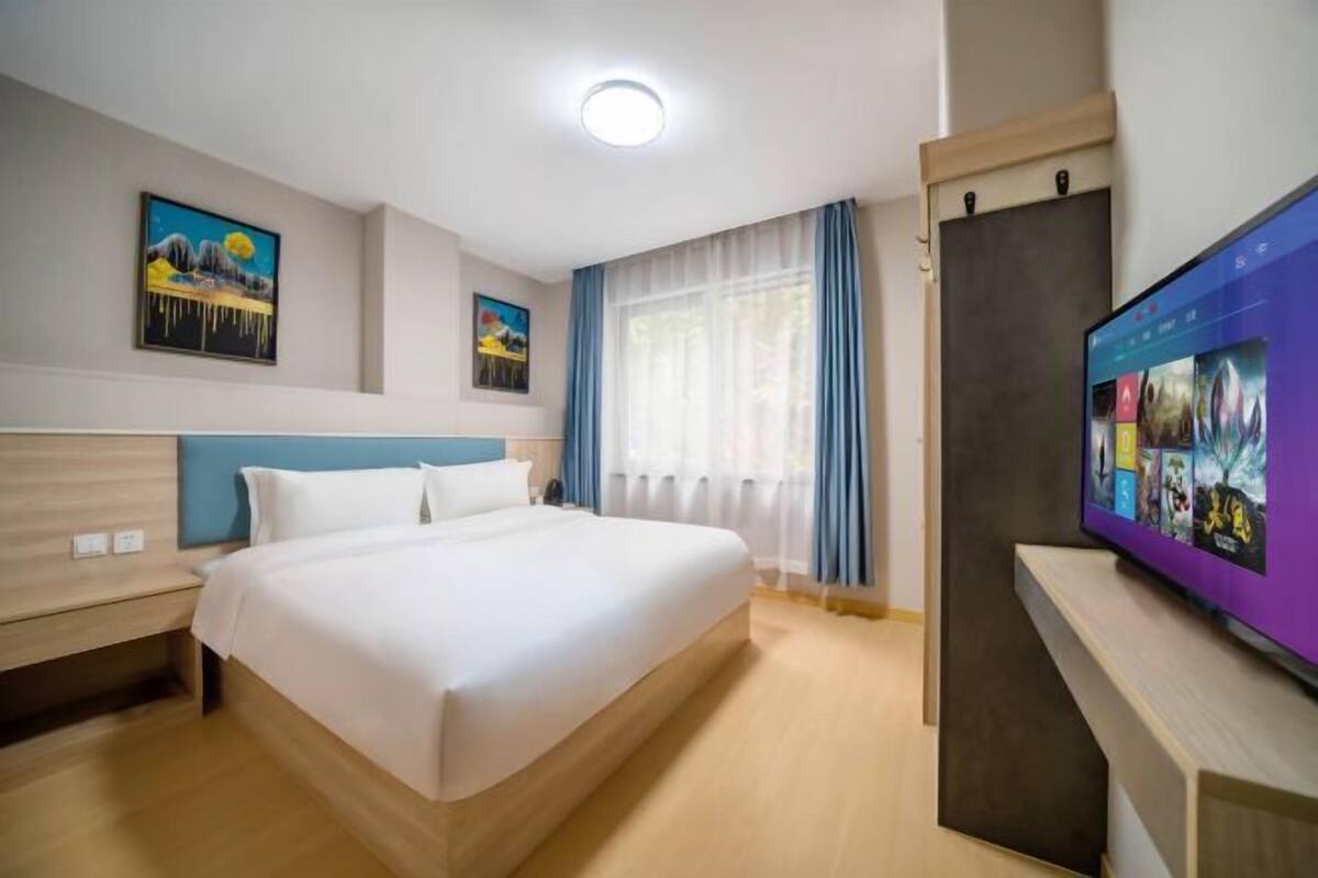 A hotel room with a large bed, a desk with a computer, a TV, and two paintings on the wall.