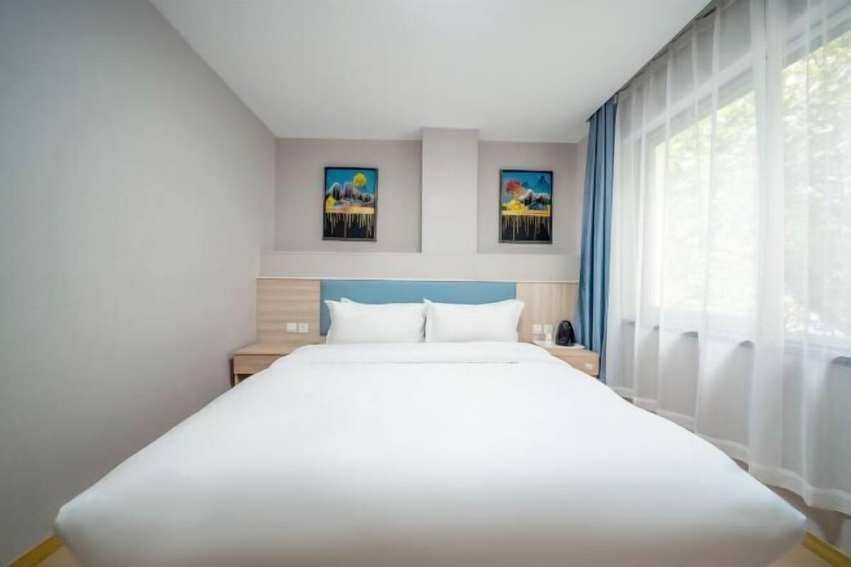 A hotel room with a large bed, two nightstands, a headboard, and two wall-mounted paintings.