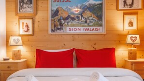 Et hotelværelse med en seng, røde puder, hvide håndklæder og et billede af en schweizisk landsby.