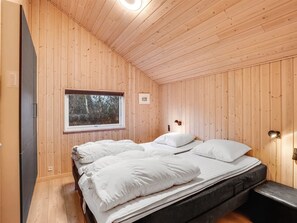 Un dormitorio con paneles de madera, una cama, un ventanal y una mesita de noche.