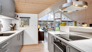 A modern kitchen with stainless steel appliances, wooden flooring, and large windows offering views of the outdoors.