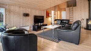 A modern living room with wooden walls and ceiling, a black leather sofa, a white coffee table, and a fireplace.