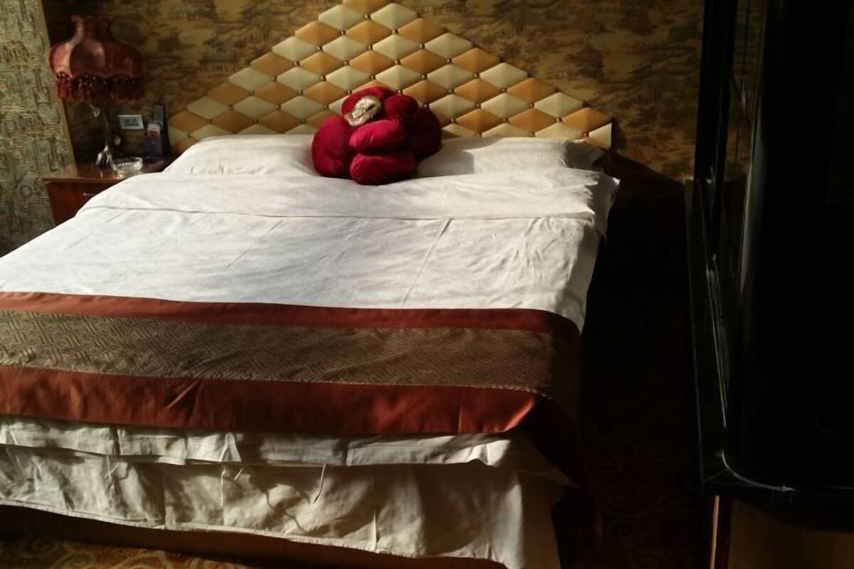 Ein Bett mit einem gemusterten Bettbezug, einem dekorativen Kopfteil und einem roten Plüschtier darauf.