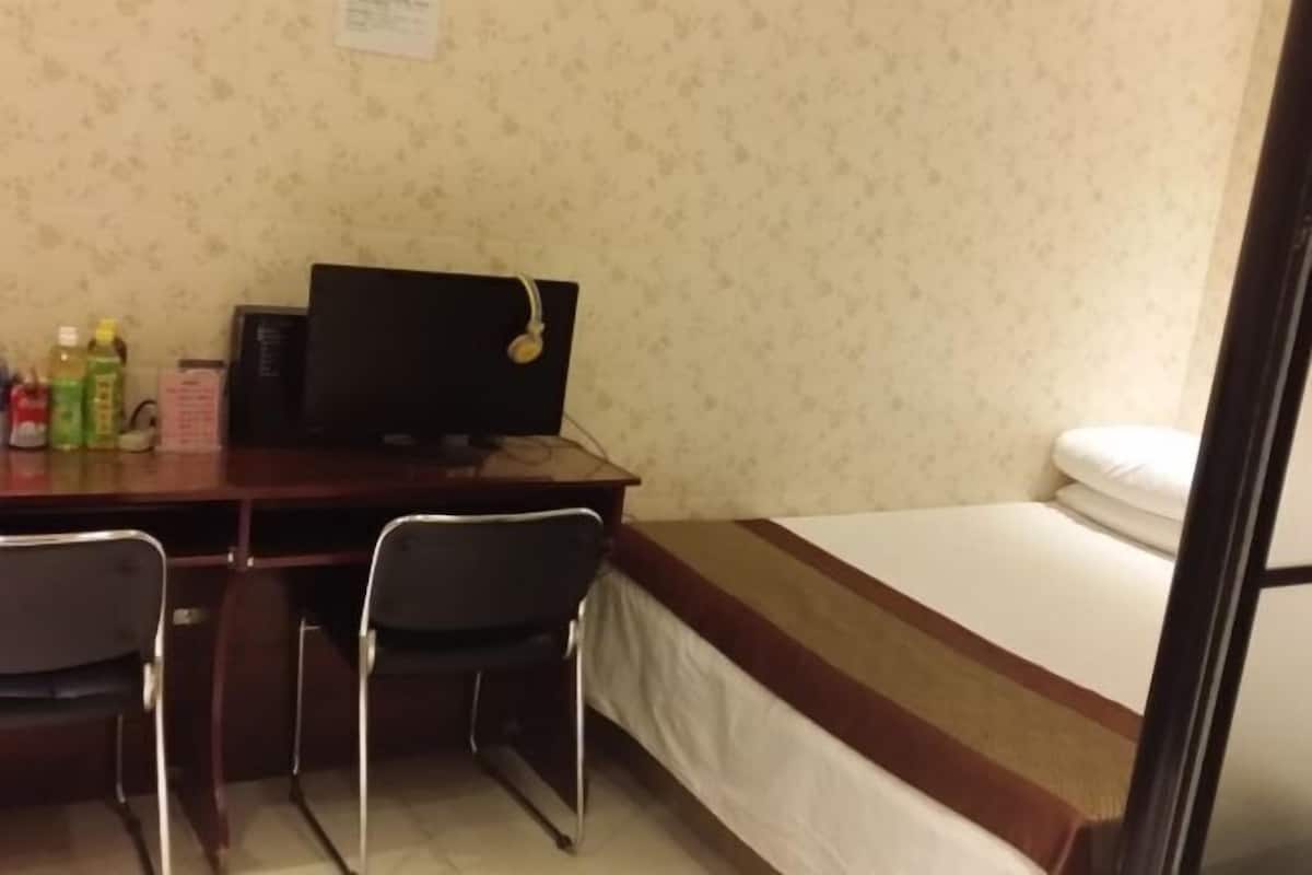 Ein Zimmer mit einem Bett, einem Schreibtisch mit Computer, zwei Stühlen und einem kleinen Tisch mit Flaschen.