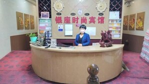 A reception desk with a woman standing behind it, surrounded by framed certificates and awards. - qinggangxian yinzuo shishangbinguan (Qinggang)