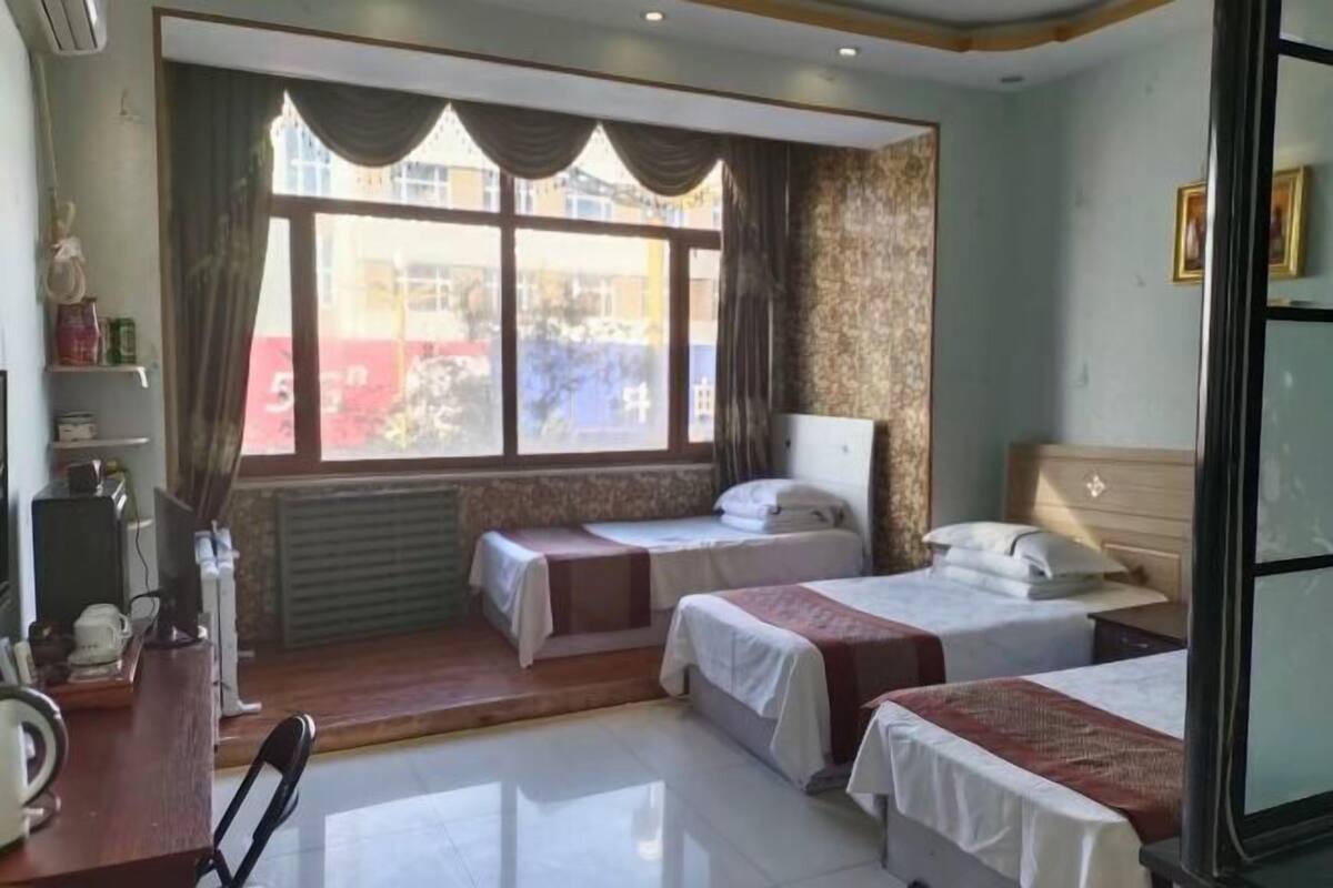 Ein Hotelzimmer mit zwei Betten, einem Schreibtisch mit Stuhl, einem Fenster mit Vorhängen und einem Heizkörper.