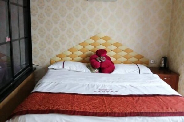 A neatly made bed with a patterned headboard, a red plush toy on the pillows, and a wooden nightstand with a bottle. - qinggangxian yinzuo shishangbinguan (Qinggang)