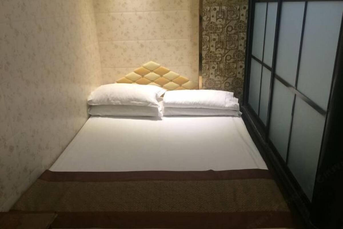 Ein Einzelbett mit Kopfteil, einer Wand mit Muster und einem Fenster mit Gitterstruktur.