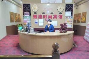 A reception desk with a counter, a computer, and a decorative item. There are framed pictures on the wall and a plant on the counter.