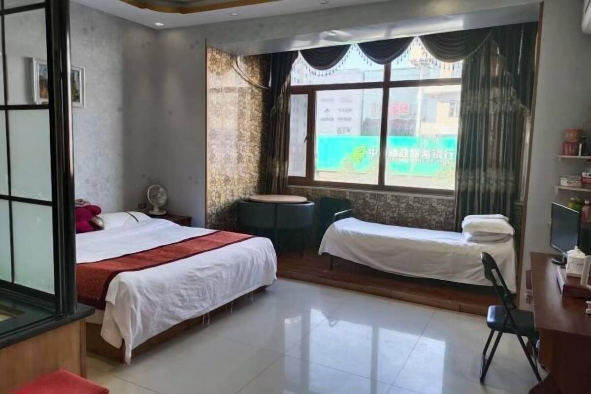Ein Hotelzimmer mit zwei Betten, einem Schreibtisch, einem Stuhl, einem kleinen Tisch und einem Fenster mit Vorhängen.