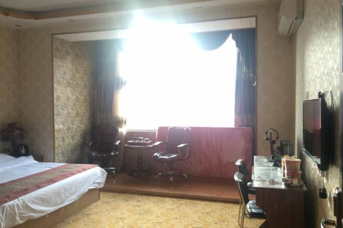 Ein Hotelzimmer mit einem Bett, einem Schreibtisch mit Stuhl, einem Fernseher und einem Fenster mit Vorhängen.
