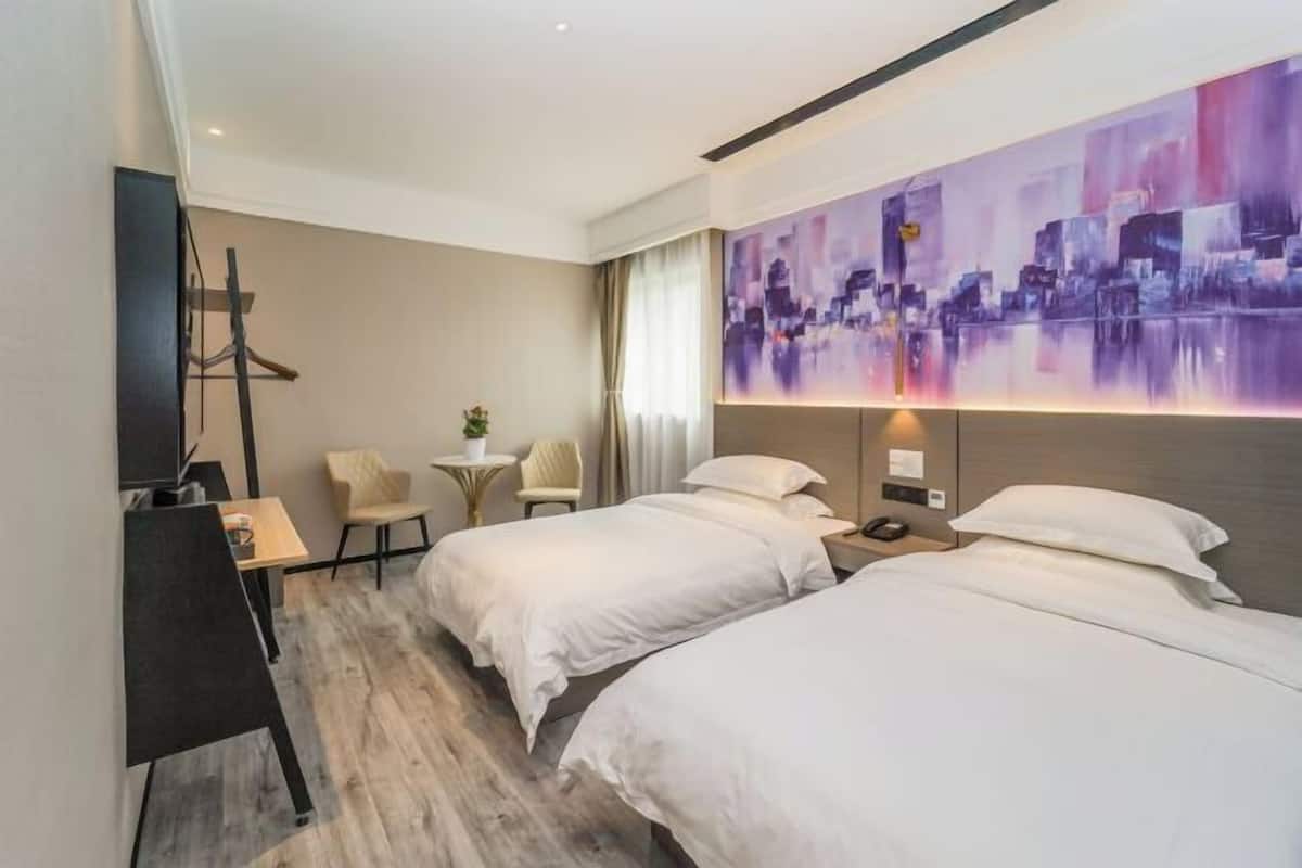 A hotel room with two beds, a desk, a chair, a TV, and a large abstract painting on the wall.