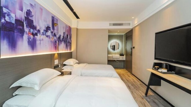 Een moderne hotelkamer met twee bedden, een grote televisie, een schilderij aan de muur, en een badkamer die door een open deur zichtbaar is.