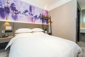Et moderne hotelværelse med en stor seng, et bybillede på væggen, en lille plante på natbordet og et skrivebord med telefon og lampe.