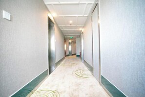 Un long couloir étroit, typique d’un hôtel, avec un sol recouvert de moquette et un mur de couleur claire.