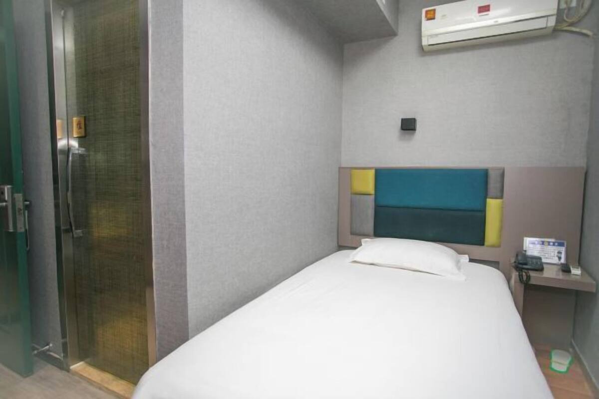 A hotel room with a bed, a bedside table with a phone, and a wall-mounted air conditioner.