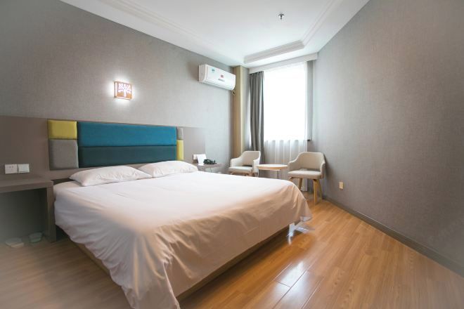 A hotel room with a large bed, a bedside table, a chair, a small table, and a window with curtains.