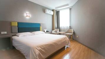 A hotel room with a large bed, a bedside table, a chair, a small table, and a window with curtains.