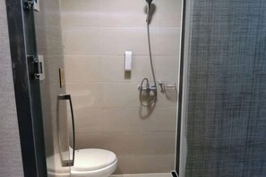 Une salle de bain comprenant des toilettes, une douche avec un pommeau de douche amovible et une paroi de séparation en verre.