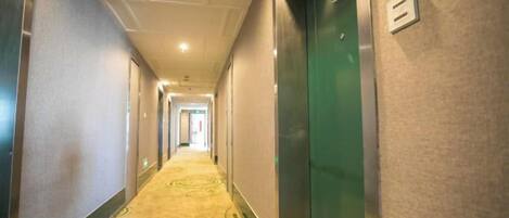A hotel hallway with carpeted floors, doors on both sides, and a light switch on the wall.