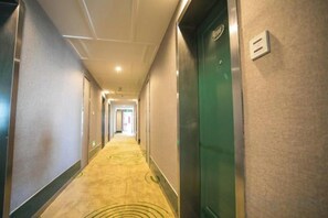 Ein Hotelgang mit Teppichböden, Türen an beiden Seiten und einem Lichtschalter an der Wand.