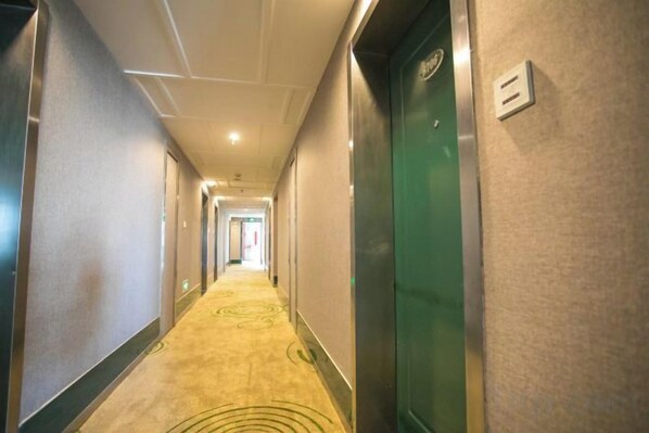 A hotel hallway with carpeted floors, doors on both sides, and a light switch on the wall. - Xinrenren hotel (Shanghai)