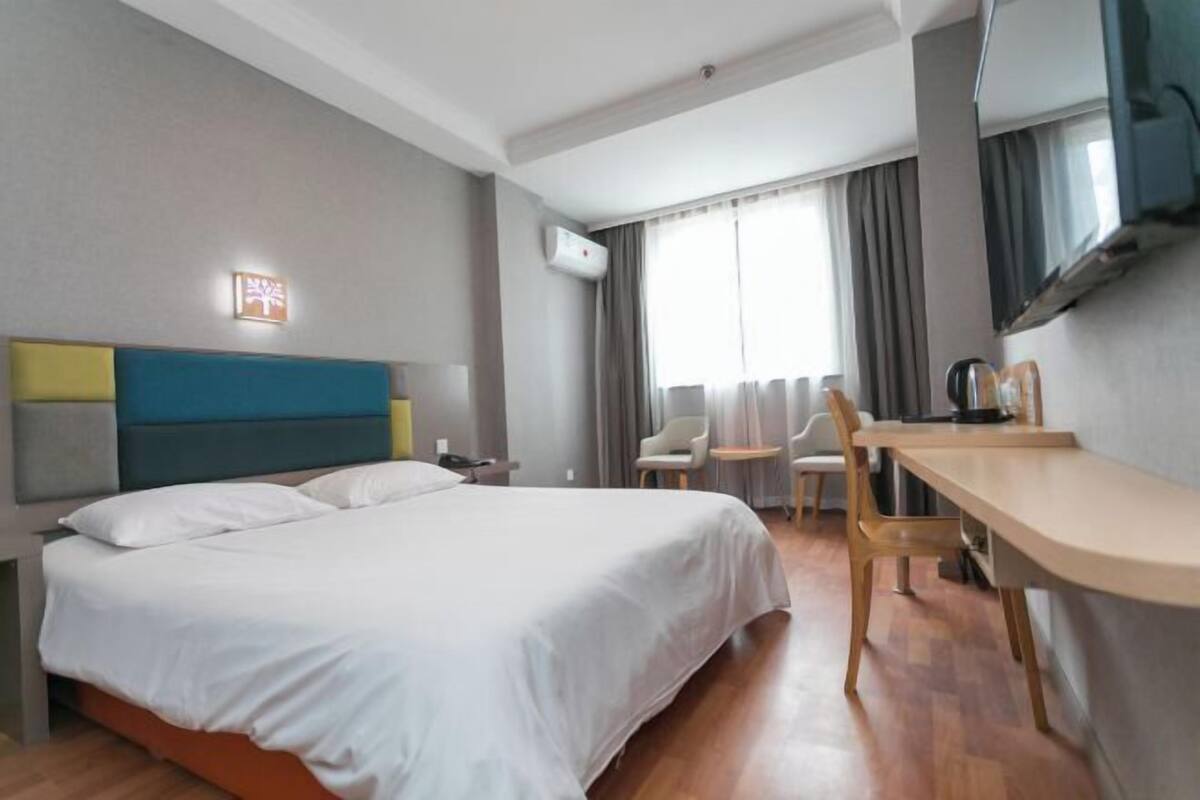 A hotel room with a bed, a desk, a chair, a TV, and a window with curtains.