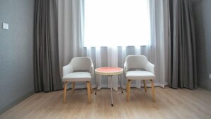 A room with two white chairs, a small round table, and a large window with grey curtains. - Xinrenren hotel (Shanghai)