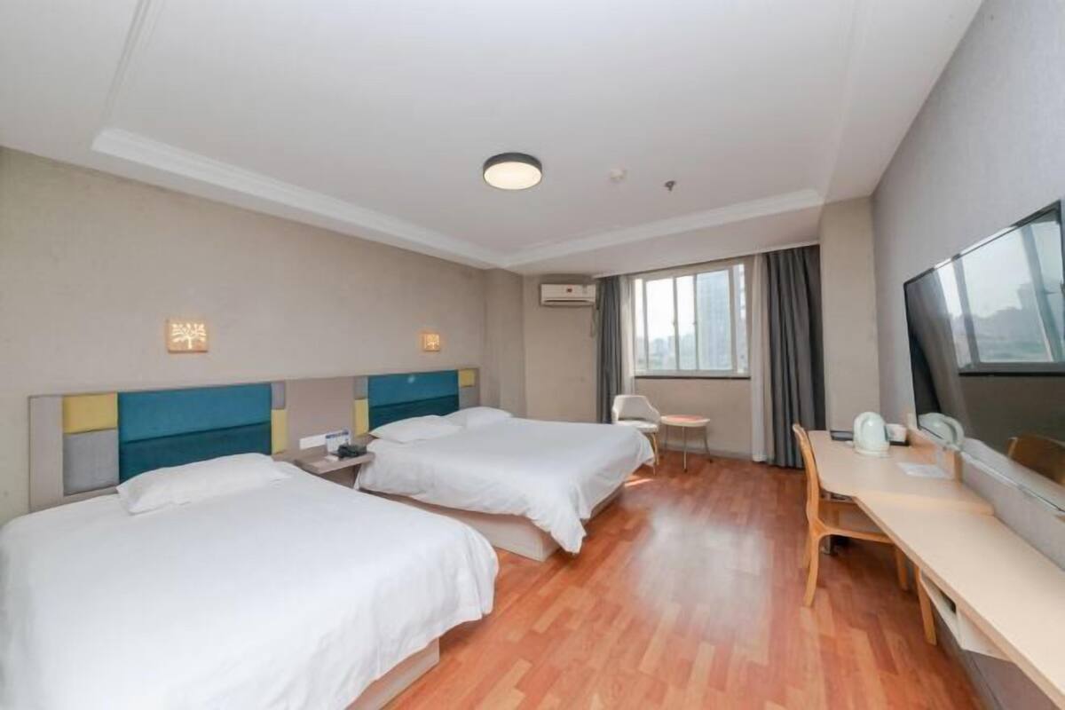 A hotel room with two beds, a desk, a chair, a TV, and a window with curtains.