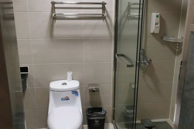 Un baño con inodoro, cabina de ducha de vidrio y un cubo de basura.