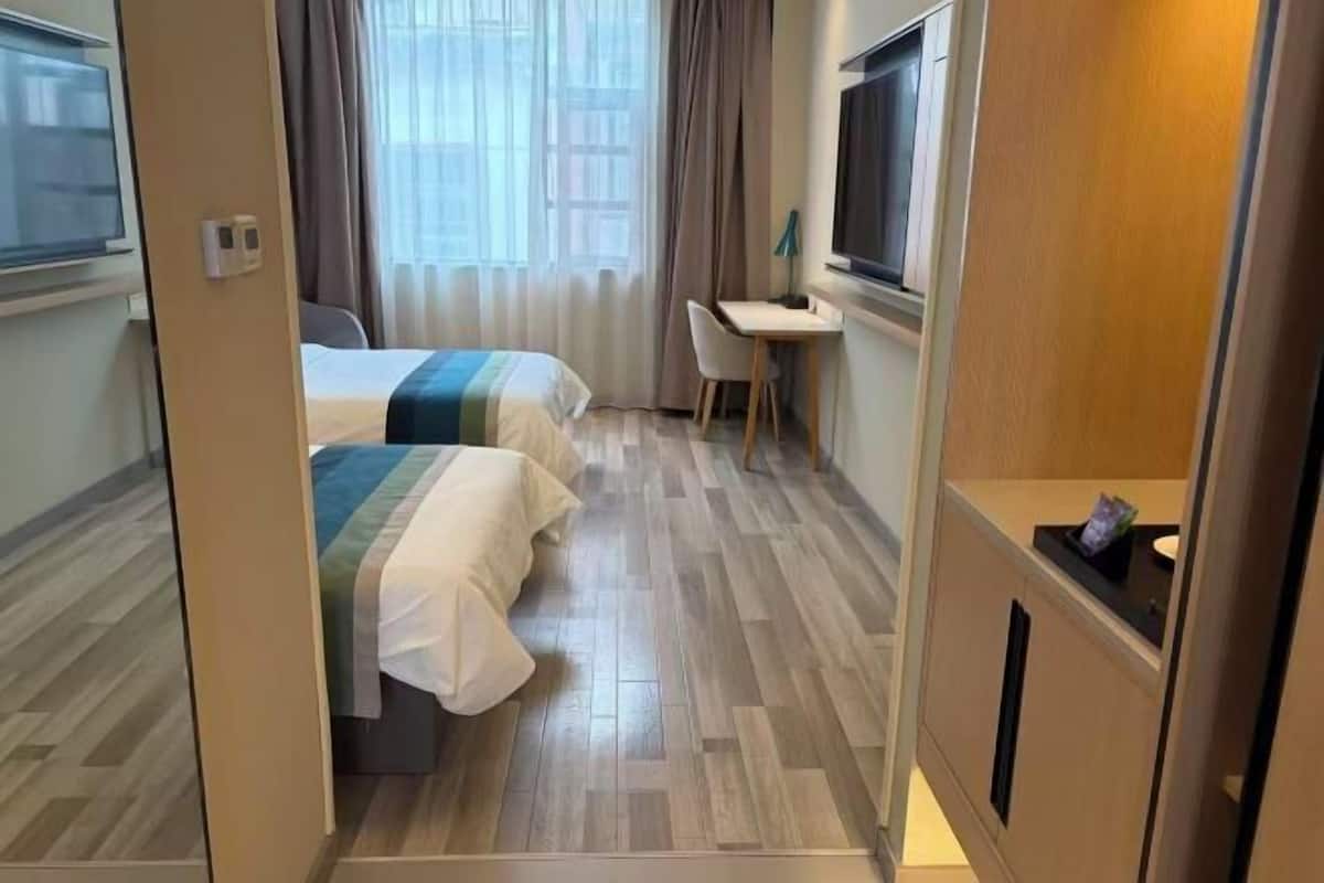 A hotel room with two beds, a desk, a TV, and a window with curtains.