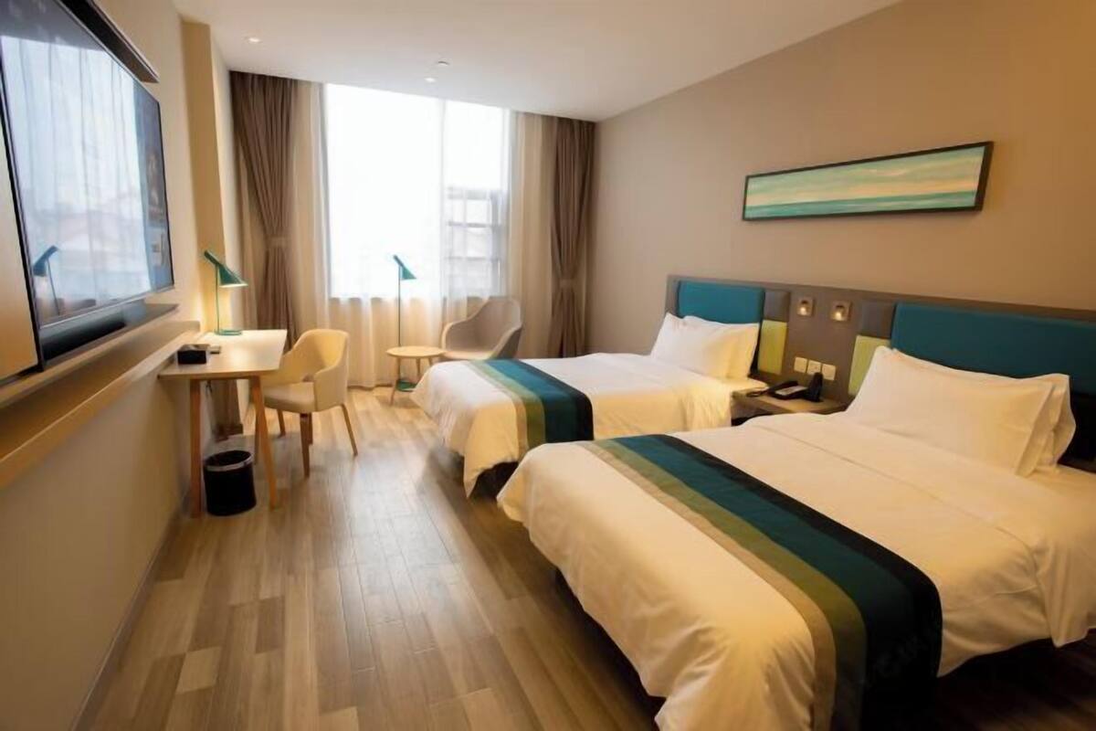 A hotel room with two beds, a desk, a chair, a TV, and a window with curtains.