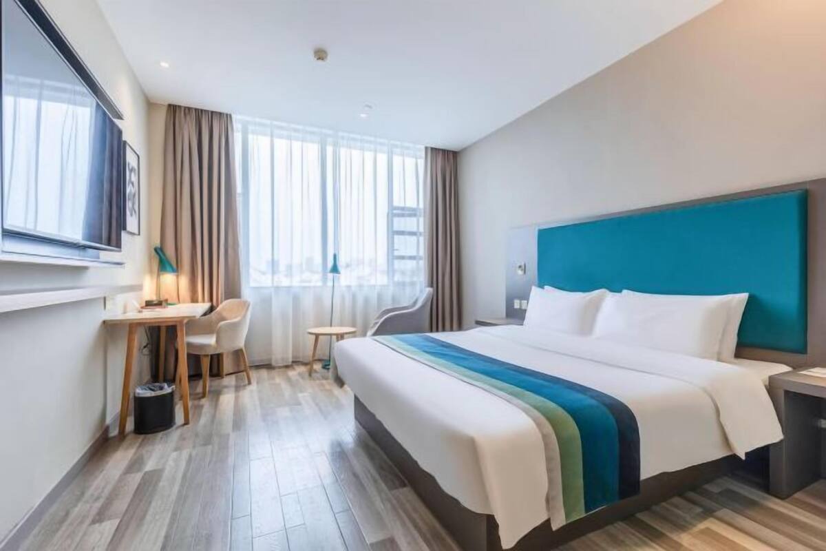 A hotel room with a bed, a desk, a chair, and a TV.
